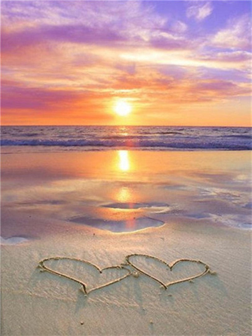 Diamond paint med to hjerter tegnet i sand ved vandkanten.
Solnedgang over vandet.