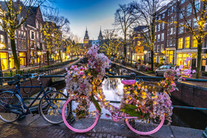 Diamond paint af en lyserød cykel, der er dækket af blomster. Placeret på overgangsbro i en by.