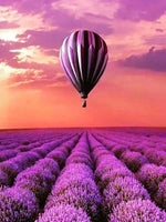 Diamond painting af lilla luftballon over lavendelmark. Himmelen er i orange nuancer.