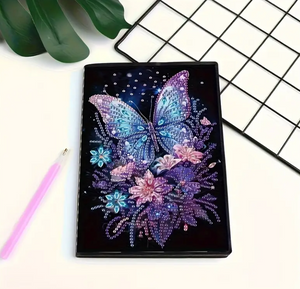 Diamond art notesbog med en sommerfugl omgivet af blomster. Blå, lilla og pink farvetoner.