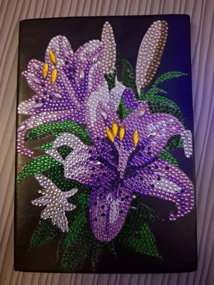 Diamond paint notesbog med lilla liljer dekoreret med glimmerperler.