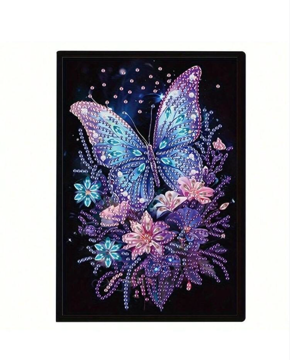 Diamond painting notesbog med en sommerfugl omgivet af blomster. Blå, lilla og pink farvetoner på sort baggrund.