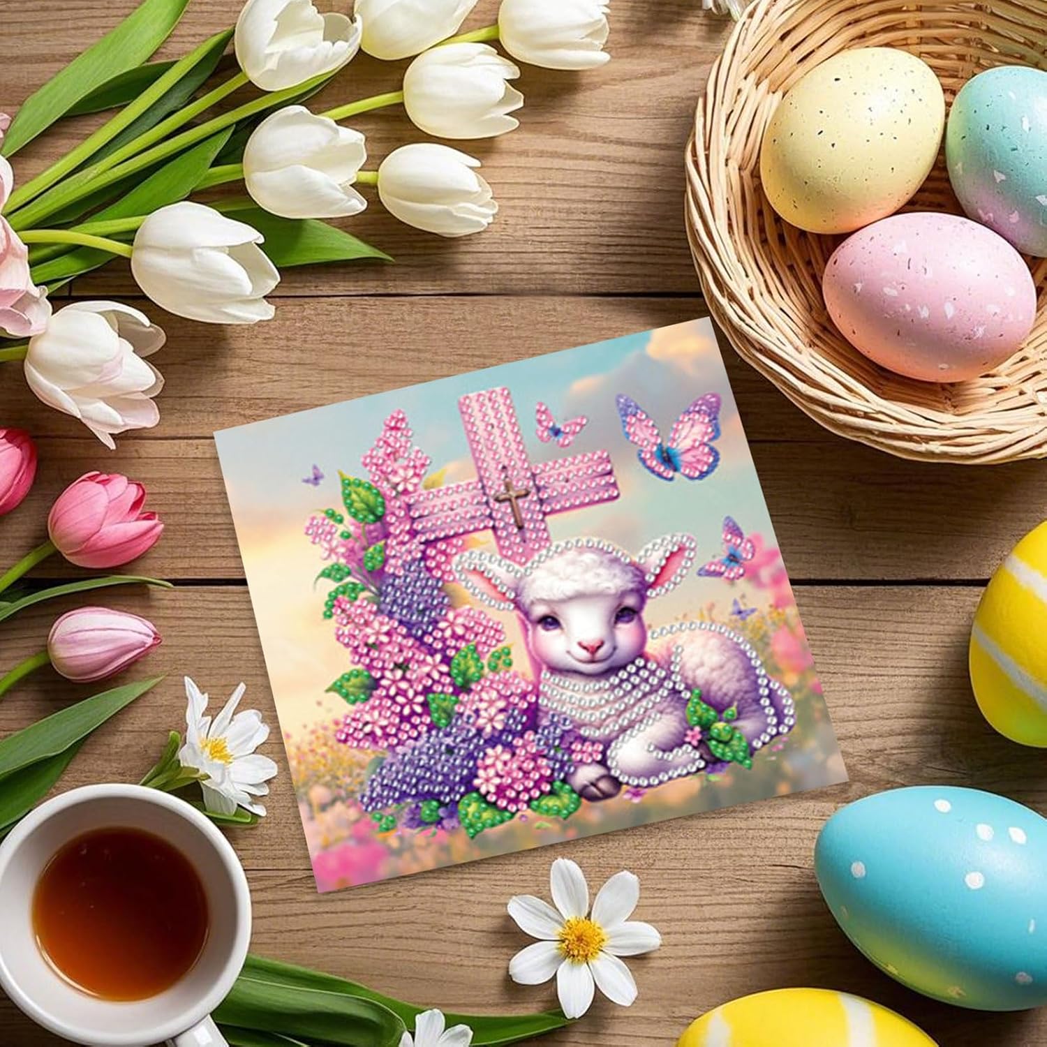 Diamond painting kort med hvidt lam omgivet af lilla og lyserøde blomster. Lyserødt kors i baggrunden. Foldbart.