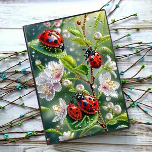 Diamond art notesbog med mariehøns omgivet af blomster.