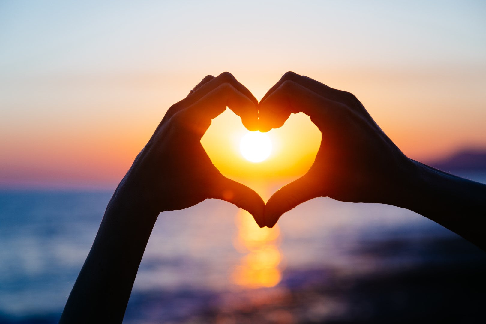 Diamond paint med hænder formet som et hjerte omkring solen ved solnedgang.