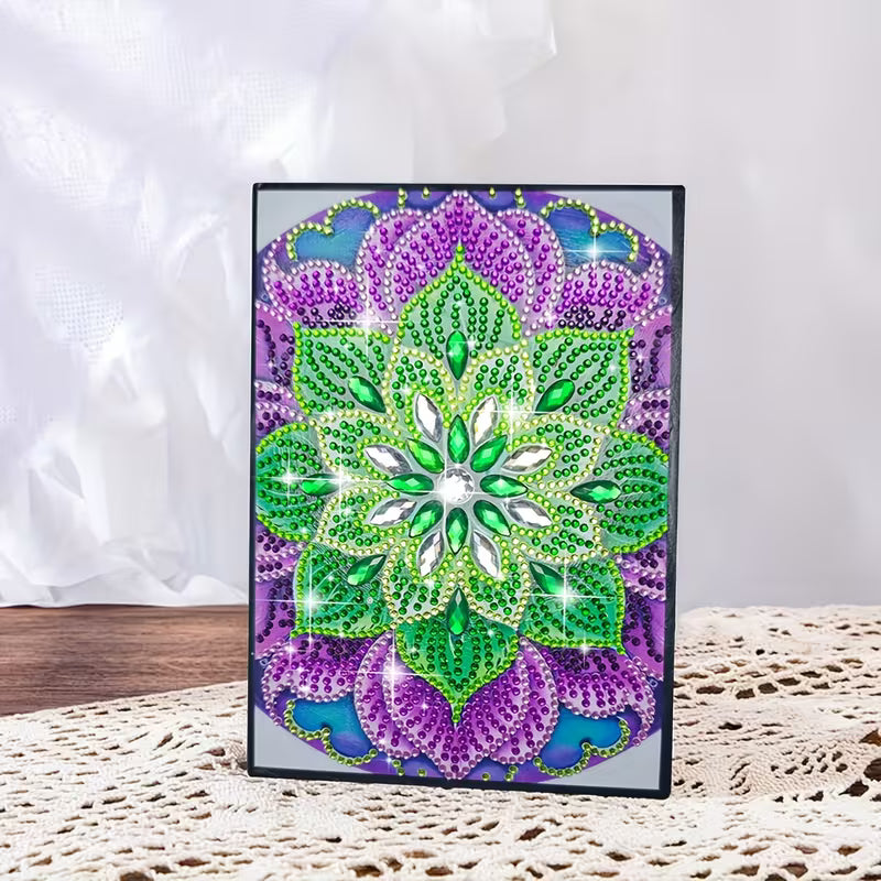 Diamond art notesbog med mandalamønster i grønne, lilla og blå nuancer.