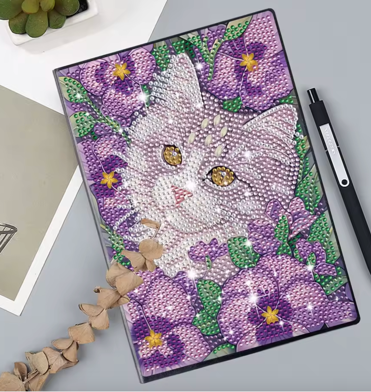 Diamond paint notesbog med en kat omgivet af lilla blomster.